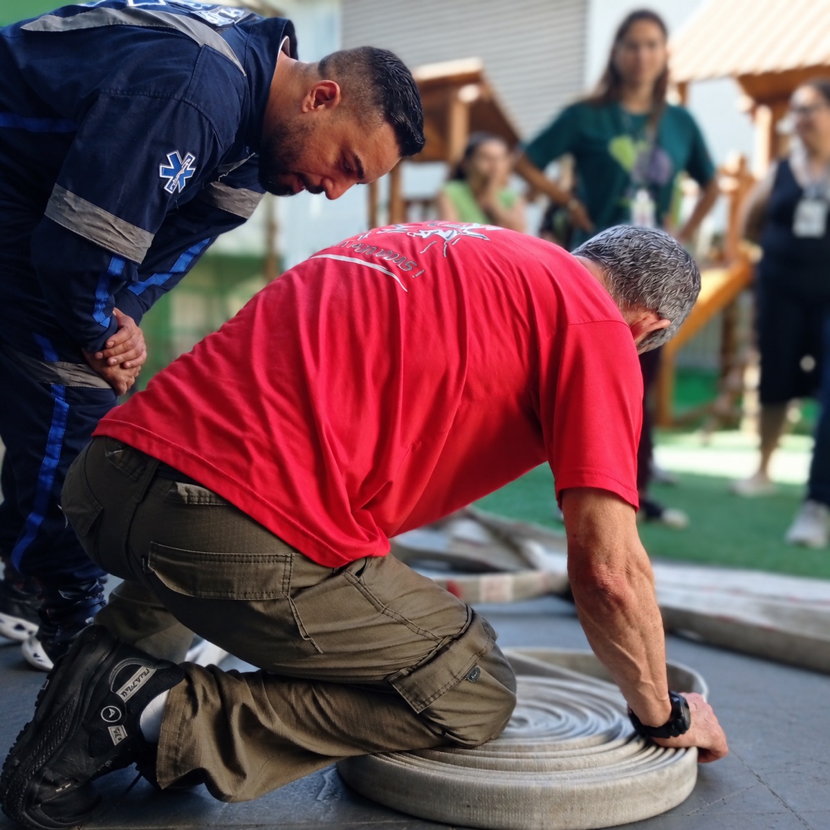 Participante pratica o manuseio de mangueira de incêndio com orientação do instrutor
